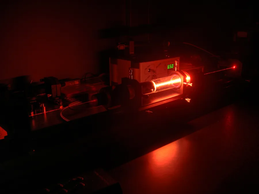 A helium-neon laser in operation, glowing orange-red in a darkened lab.