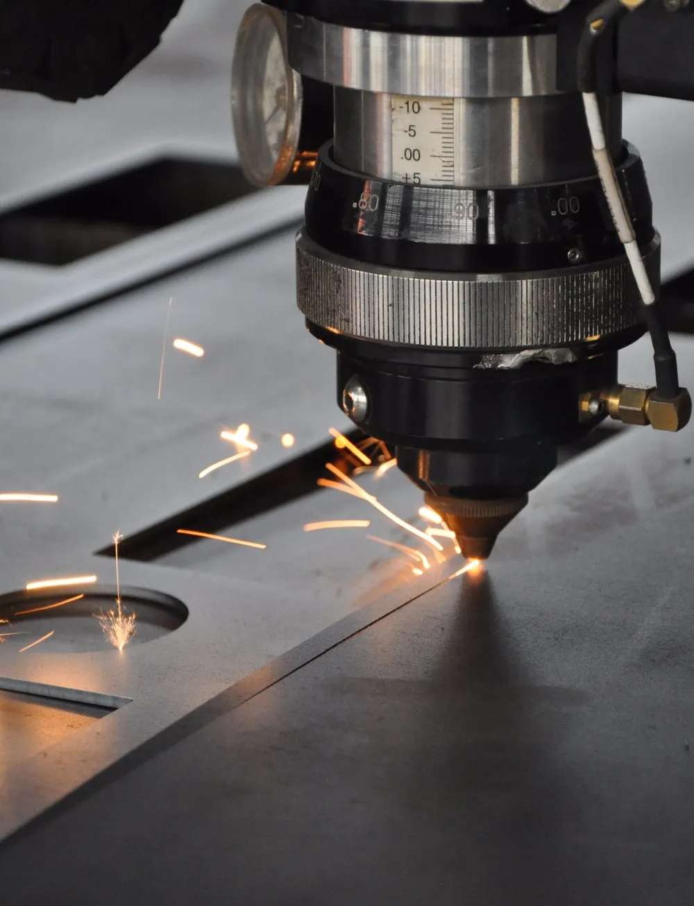 A laser cutting machine slicing through a metal sheet, throwing off bright sparks.