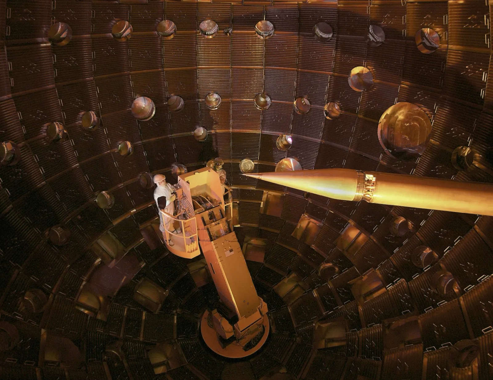 Inside the National Ignition Facility target chamber. A technician stands on a platform for scale, dwarfed by the massive spherical chamber lined with laser beam ports.